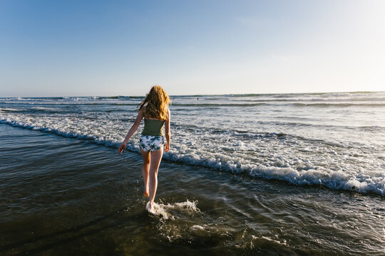 Teen girl walking in swimsuit in ocean with waves at the beach
