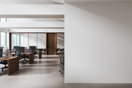 Modern office workspace with wooden desks and chairs beside large empty white wall for interior design mockup or poster template concept. 3D Rendering