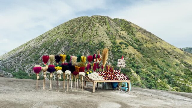 Bright decorative flower stand with colorful bouquets of Javanese Edelweiss located on an elevated viewpoint at Mount Bromo Indonesia overlooking volcanic hills and rural mountain scenery.