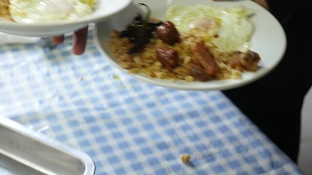 Close-up of a waiter holding two plates of traditional Spanish migas with fried eggs, peppers and chorizo.