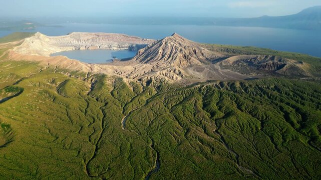 Smooth side glide drone shot circling Taal Volcano crater, highlighting rugged terrain, lake textures, and volcanic formations.