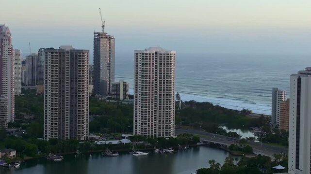 Drone footage sweeping left over the Nerang River near Budds Beach, revealing waterfront high-rise towers with the coastline in the distance.
