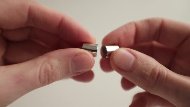 A close-up, first-person perspective video of a pair of hands demonstrating a small, cylindrical silver magnetic clasp (often called a barrel or tube clasp) used for jewelry making.