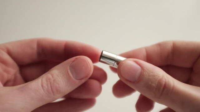 A close-up, first-person perspective video of a pair of hands demonstrating a small, cylindrical silver magnetic clasp (often called a barrel or tube clasp) used for jewelry making.