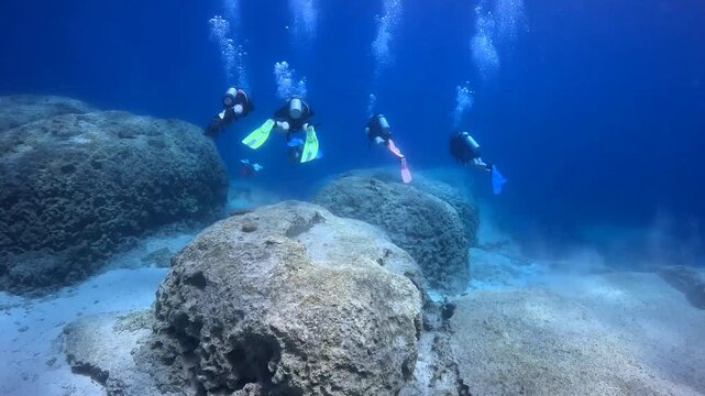 Scuba divers swimming and exploring rocky shallow seascape in the clear sea. Underwater video from scuba diving. Beautiful seascape with the divers, travel video. Tourists swimming in the ocean.