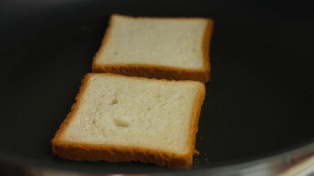 Hand puts two slices of white bread in the pan to toast, close up