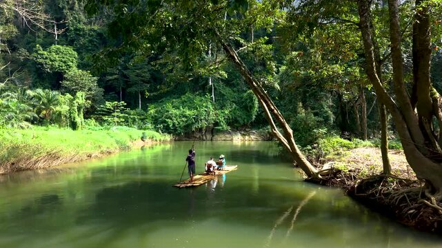 Amidst the stunning greenery of Khao Sok National Park, two adventurers glide on a traditional bamboo raft. The serene river reflects the vibrant jungle, creating a peaceful escape in Thailand.