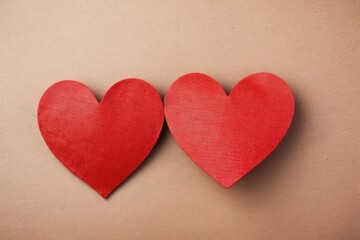 Fototapeta premium Two red heart shapes resting on a light brown background, representing romance