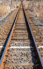 Obraz premium Close-up of a straight single railway track with rusty rails and withered grass in the countryside.