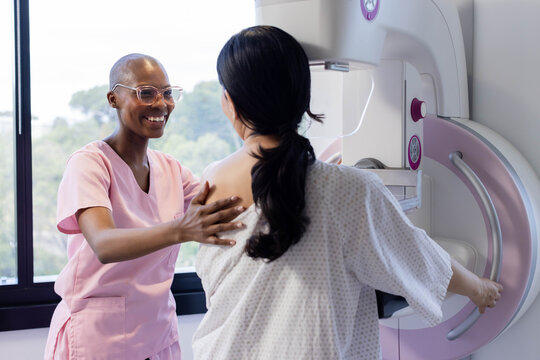 Female mammography tech in pink scrubs and patient positioning at mammography unit, holding handle