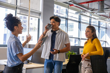 Obraz premium Diverse coworkers gathering near monitors in open office, gesturing, sipping mug and holding tablet