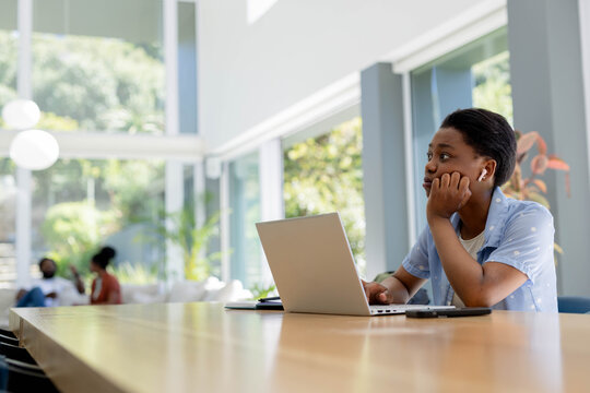 Family youth sitting at long wooden table on right, working on laptop with notebook, copy space