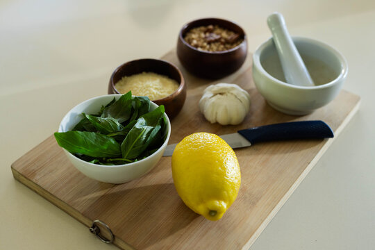 Whole lemon sitting on wooden cutting board with basil, paring knife, garlic, mortar