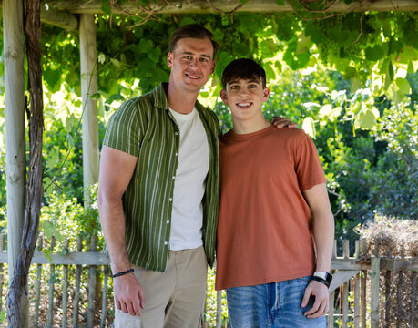 Father and teen son standing under wooden pergola covered in vines, wearing bracelet and smartwatch