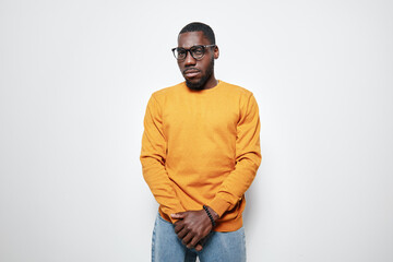 Obraz premium African American man with dark skin wearing glasses and orange sweater standing against white background looking thoughtful and serious in casual style portrait.
