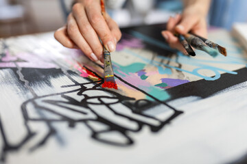 Naklejka premium Artistic close-up of a woman's hand painting red details on an abstract canvas, female painter holding several brushes while working in her studio, creative entrepreneurship and craft concept.