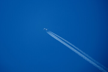 Military Transport Aircraft Flying in Clear Blue Sky with Long White Contrail. Strategic Cargo Plane Cruising at High Altitude Leaving Vapor Trail