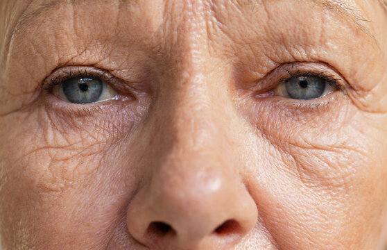 Close-up face is revealing detailed wrinkles, pores, light blue-gray eyes in soft-lit studio