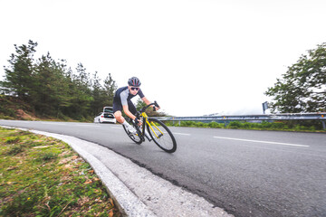 Fototapeta premium Young caucasian man going downhill on a corner with a road bike on an asphalt road of a mountain.