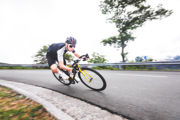 Fototapeta premium Young caucasian man going downhill on a corner with a road bike on an asphalt road of a mountain.