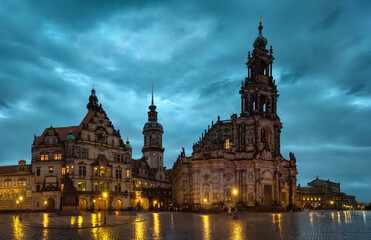 Evening view of Dresden Cathedral and historic buildings at Theater Square with illuminated baroque architecture and wet cobblestone reflections in the old town of Saxony, Germany