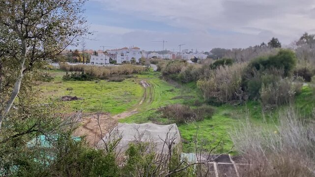 Urban residential area bordering an undeveloped overgrown field with a dirt track, showcasing environmental impact and growth