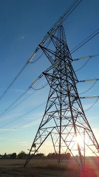 Industrial silhouette of a power pylon under a glowing sunset horizon in the British landscape representing national energy infrastructure and supply.