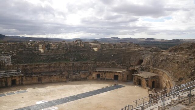 Panorama: Roman amphitheatre at Uthina archaelogical site in Tunisia under dramatic storm clouds, ancient stone architecture, symmetry, and the monumental scale of this UNESCO World Heritage landmark
