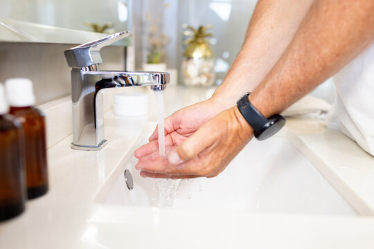 Cupped hands are catching water from chrome faucet at bathroom sink, amber bottles nearby