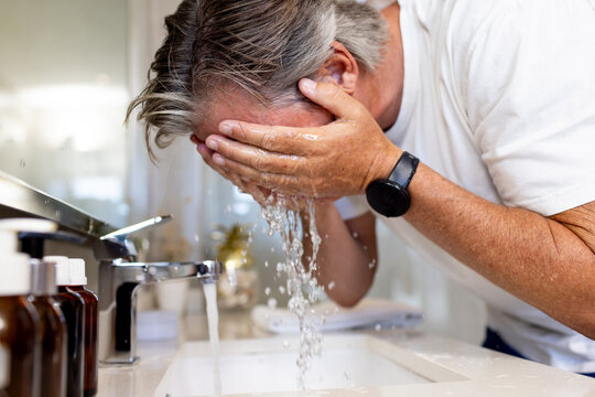 Chrome faucet is running and water is splashing into sink on vanity, amber bottles reflecting