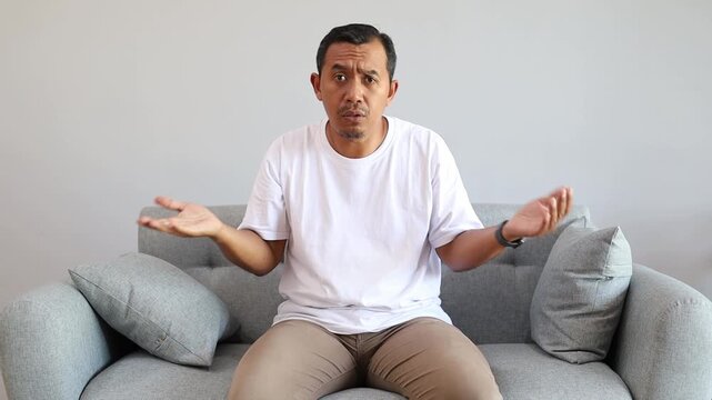Confused Asian handsome man feeling embarrassed about ambiguous question, having doubts, no idea, being clueless and uncertain at home