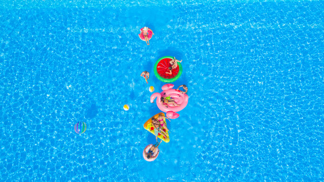 AERIAL: Cheerful young friends having a watergun fight on fun floaties in pool