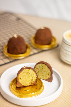 Close up of Dubai Chewy Cookie sliced, showing a rich pistachio and kataifi filling inside, coated with coated powder and served on elegant gold base. Artisan gourmet pastry paired with latte coffee i