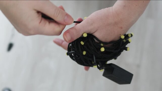 Smart Storage features hands coiling black string lights with yellow bulbs into neat bundle. Efficient Smart Storage technique prevents knots and tangles in holiday fairy lights for next season.