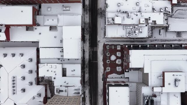 Dense downtown street in America with snow covered rooftops and roads. Urban city blocks form geometric pattern during winter snowfall, showing infrastructure and density. Aerial top down flyover shot