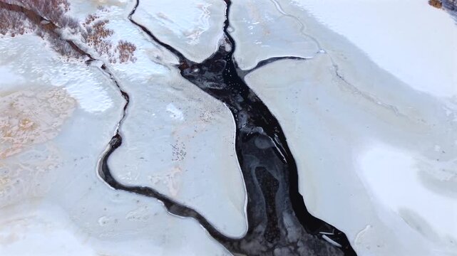 A top down view over a frozen lake with unfrozen, streams and tributaries on a sunny day in winter. The snow on lake and the water looks like marble as the camera tilted down, dolly in and boom down.