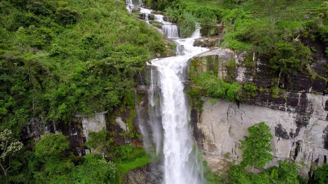 Tall Ramboda waterfall drops into green forest basin in Nuwara Eliya Sri Lanka, aerial descend