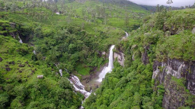Narrow Ramboda waterfall cuts through green valley forested hills in Nuwara Eliya Sri Lanka, aerial approach establish