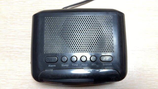 A black digital alarm clock broadcasts from an unassigned FM frequency. The internal speaker emits a harsh, constant white noise hiss and sharp electronic crackling.