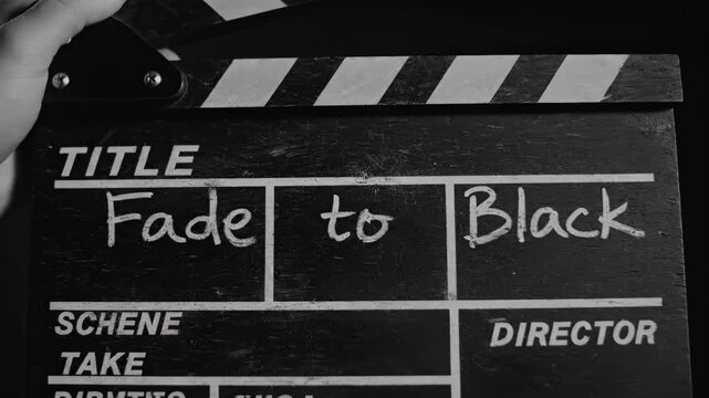 A hand holding a black film clapperboard titled Fade to Black