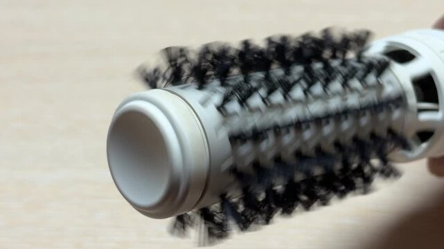 The rotating brush head of this hair styler spins smoothly against the hair. This mechanical action produces a rhythmic, low-pitched hum and a soft whirring sound of rushing air.