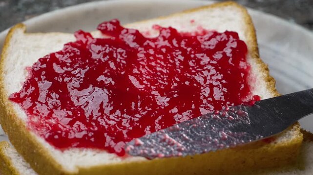 Spreading Red Jam on a Slightly Browned Toast with Table Knife on Cutting Board. A man spreading jam over a White bread slice 4k Video
