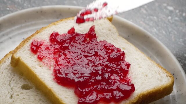 Spreading Red Jam on a Slightly Browned Toast with Table Knife on Cutting Board. A man spreading jam over a White bread slice 4k Video