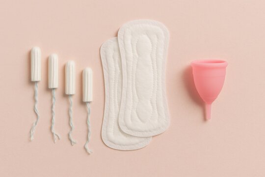 Tampons, sanitary pads and a menstrual cup on pastel background, concept of feminine hygiene, period care and sustainable menstrual products