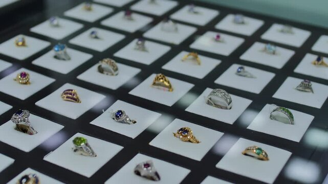 Luxury ring jewelry display with gemstone ring collection in showcase, gold silver diamond sapphire emerald ruby rings arranged in grid, retail boutique elegance concept

