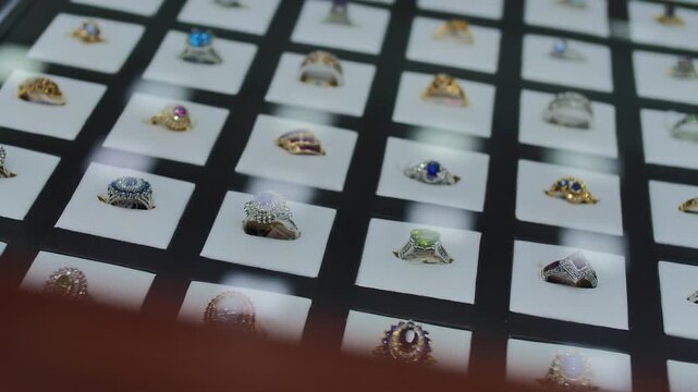 Luxury ring jewelry display with gemstone ring collection in showcase, gold silver diamond sapphire emerald ruby rings arranged in grid, retail boutique elegance concept
