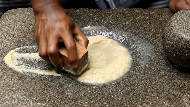 Close Up Of Hands Grinding Spices On A Stone Grinding Stone With Water And A Pestle In Natural Lighting And Rustic Kitchen Environment
