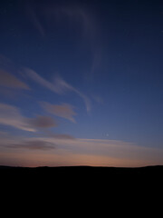 Night sky with drifting clouds and a field of stars over a quiet horizon