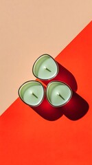 Three triangular candles with green tops create shadows on an orange and beige background, arranged in a tight cluster with defining edges highlighting modern design elements