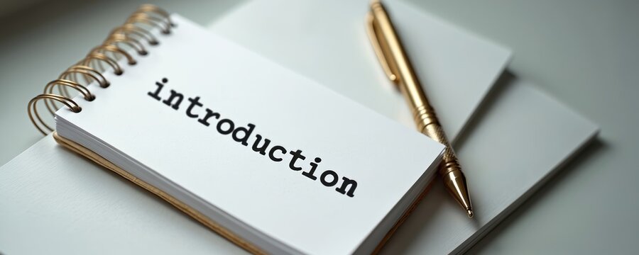 Notebook page with word introduction written. Golden pen rests on spiral bound notepad and blank paper. Beginning concept for business, marketing, or personal planning.